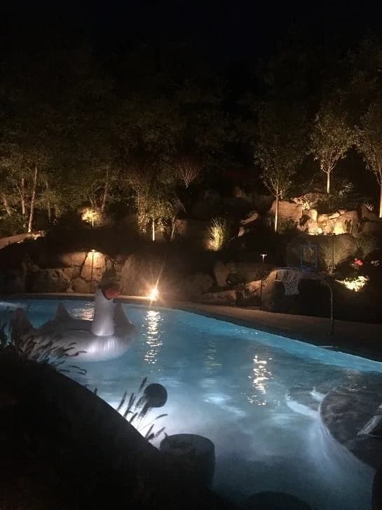 Residential inground pool at night with underwater LED lighting and landscape uplighting — wired by Priority Electric
